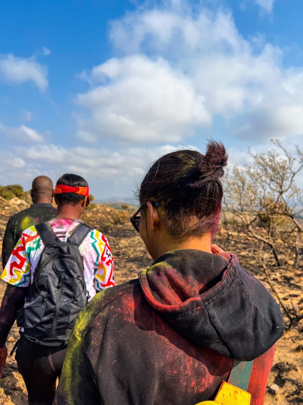 Three hikers walking away along a dusty ridge under a blue sky